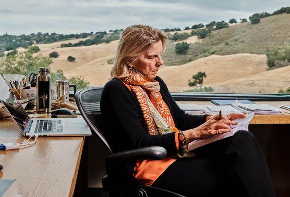 A woman sitting in her office concentrating on a book she is reading with a hillside backdrop in the background.
