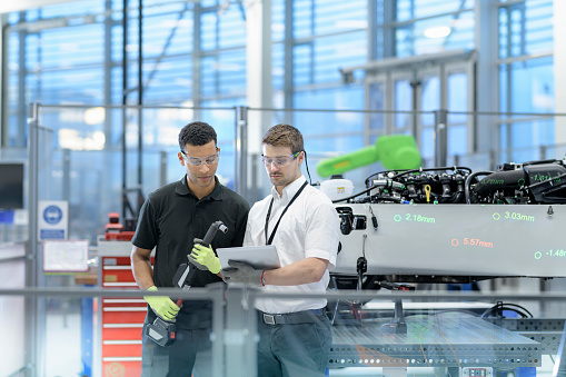 Worker in manufacturing plant holding equipment reviewing plans with manager