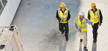 Overhead view of three workers in safety vests and hard hats walking on plant floor