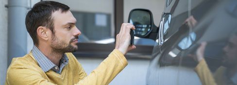Person kneeling down by car driver door to take picture with cellular telephone