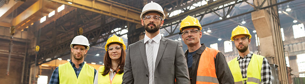 Maintenance manager and team of 4 maintenance technicians standing confidently in industrial plant
