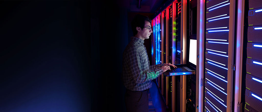 A man working at a keyboard on a rack-mounted computer in a server room.