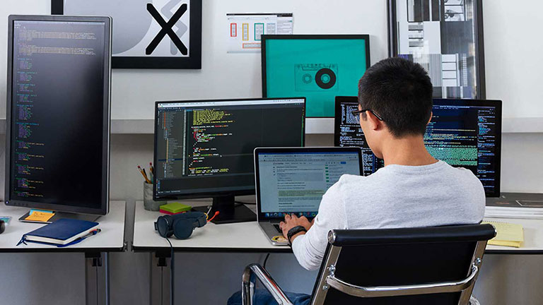 Photo of person in office working on multiple computer monitors 