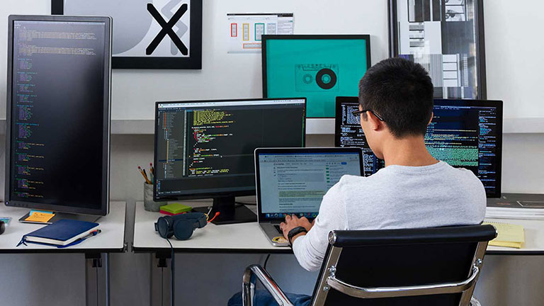 Person in office working on multiple computer monitors