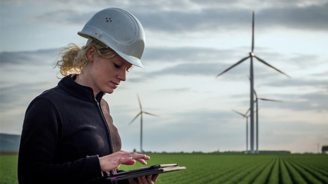 A technician using a tablet app outside in front of wind turbines