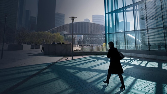 A woman walking through shadows toward a business district plaza