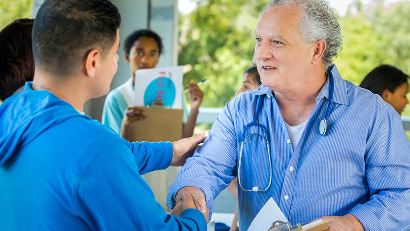 A young man in a blue hoodie thanks a volunteer doctor for his time and support at a localflu shot vaccination event