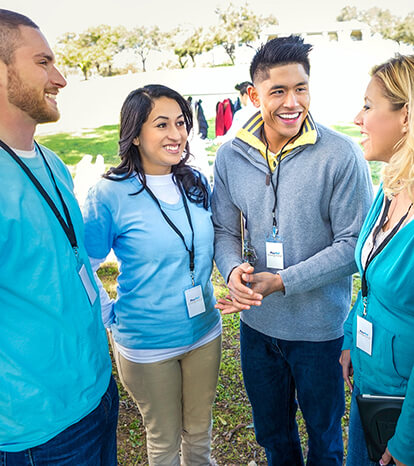 Four young volunteer workers wearing their company lanyards celebrate a successful day of giving back and helping others